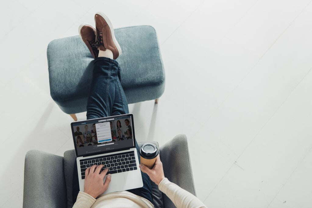 Draufsicht eines Mannes, der einen Pappbecher hält und einen Laptop benutzt - Kunden erreichen ohne jedes Mal ein Linkedin Beitrag erstellen zu müssen, Linkedin Werbeanzeigen machen das möglich