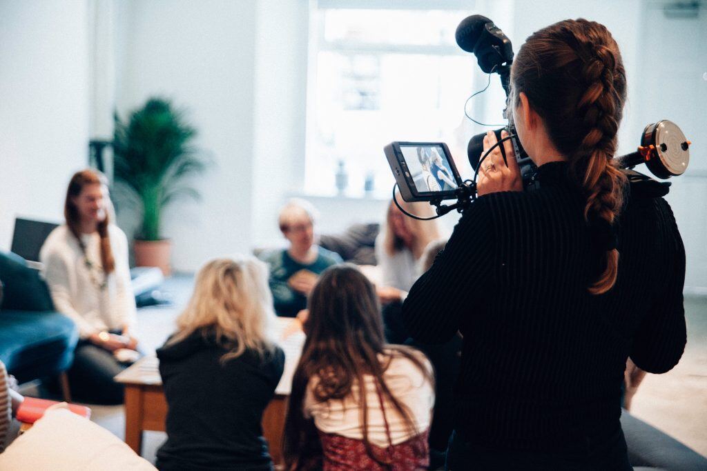 Eine Frau filmt eine Gruppe an einem Tisch - Filmproduktion und Videoproduktion für Marketing Zwecke 